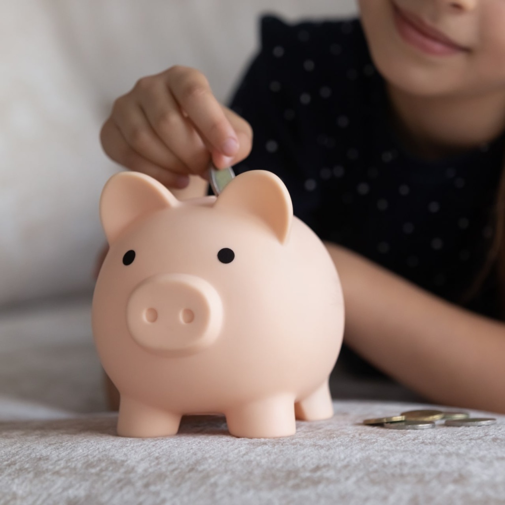 Child dropping coin into toy pink piggybank. Smart girl saving money, collecting cash for future purchase, learning economy, business, investment, counting budget. Financial planning concept. Close up