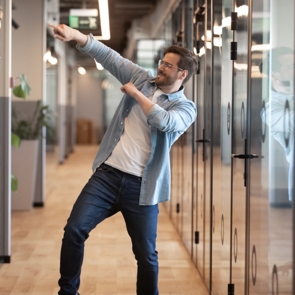 Overjoyed funny male employee have fun perform winner dance in modern office hallway, excited happy millennial businessman celebrate business success or promotion, Friday evening, end of working week