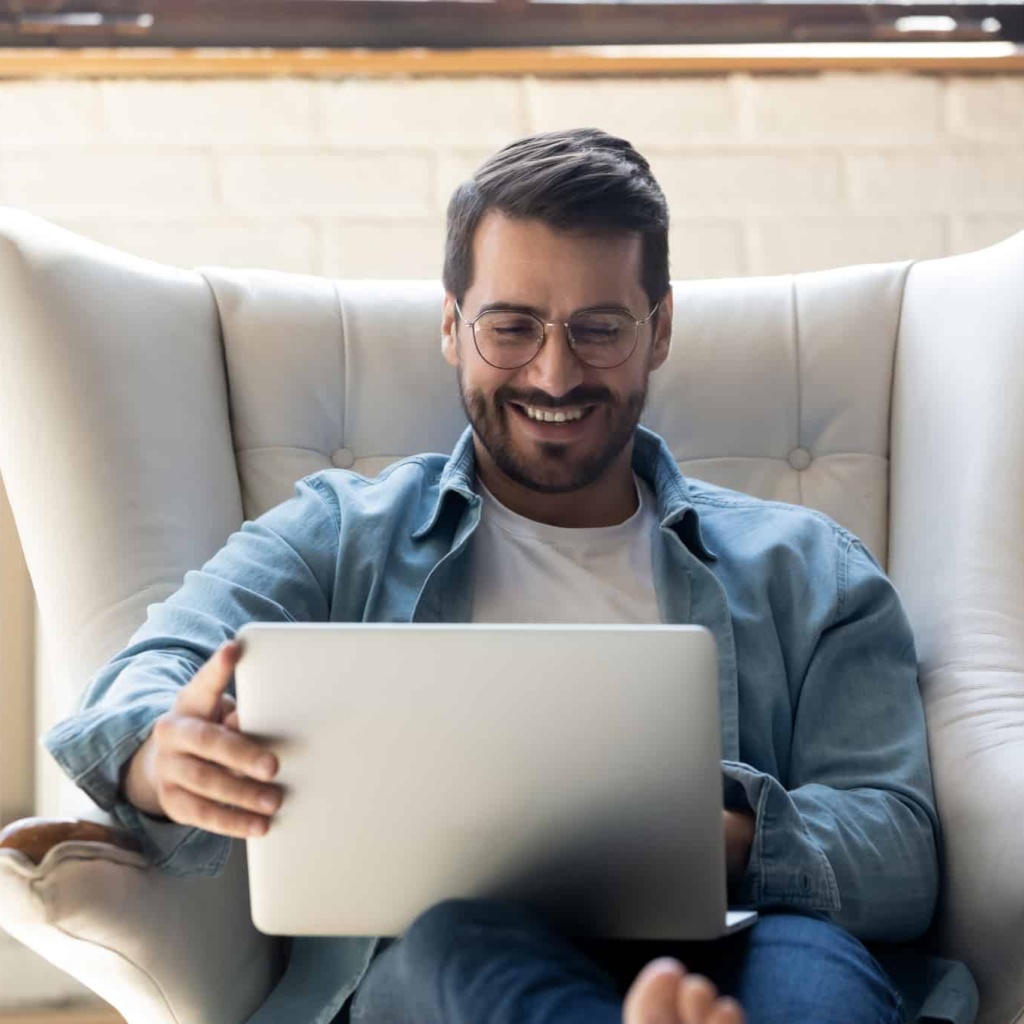 Smiling,Young,Man,Wearing,Glasses,Using,Laptop,,Sitting,In,Cozy